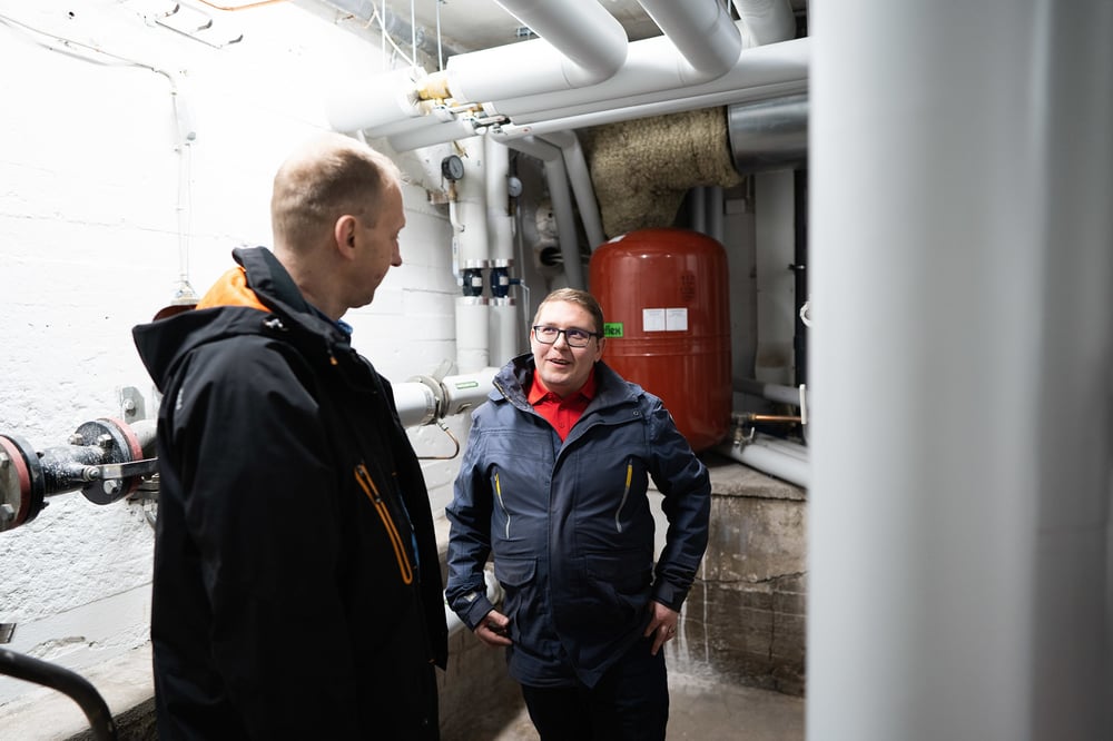 Kaksi miestä keskustelee lämmönjakohuoneessa. 